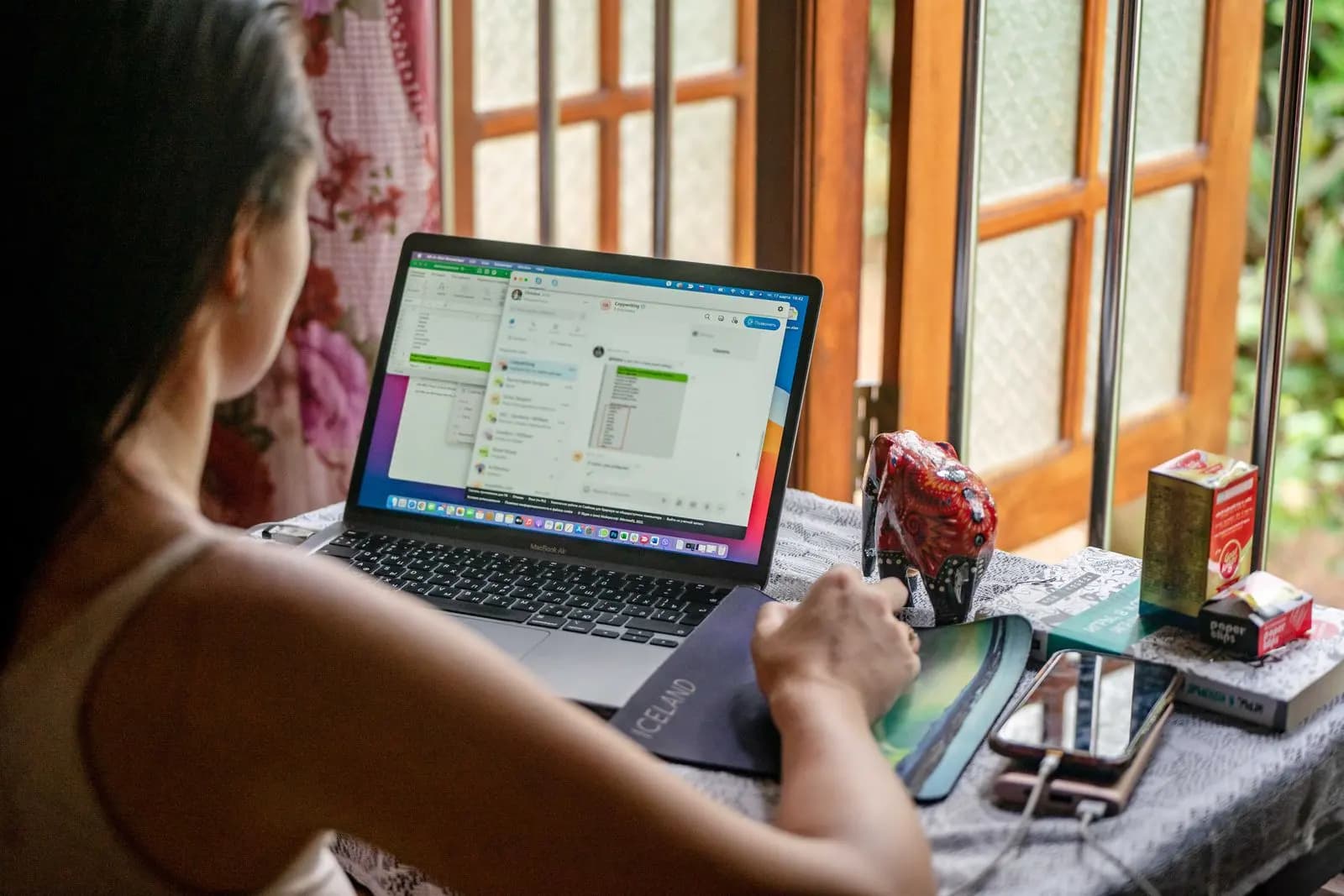 Mulher trabalhando no notebook em casa, perto de uma janela