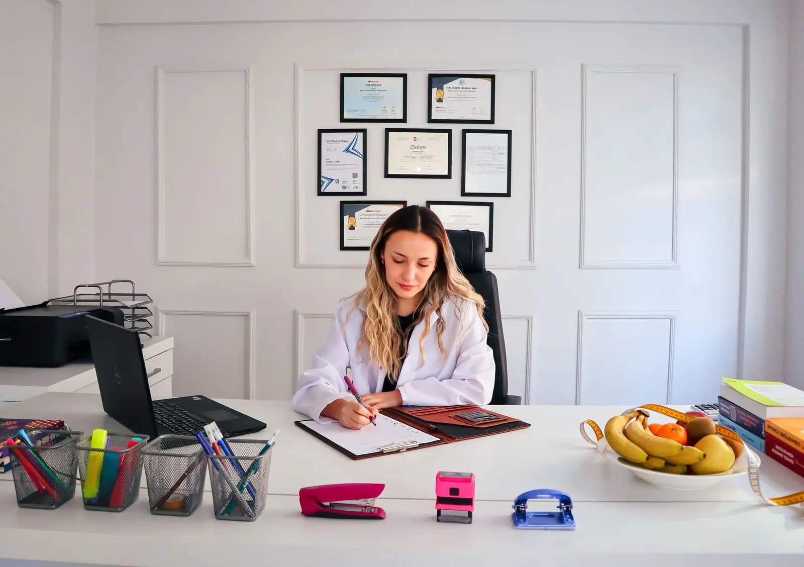 Nutricionista escrevendo à mesa de trabalho, com frutas e notebook